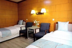 Quarto de hotel com duas camas de solteiro, uma mesinha com telefone e duas luminárias na parede.