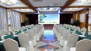 A conference room with rows of white chairs, a long table with green tablecloths, and a projector screen displaying a landscape image. - Hebei Provincial State-owned Assets Supervision and Administration Commission (Shijiazhuang)