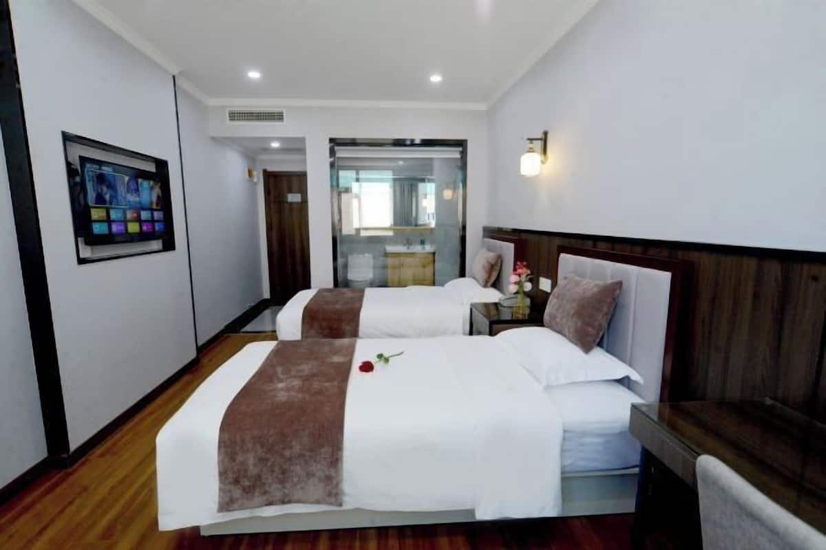 A hotel room with two beds, a TV mounted on the wall, a wooden floor, and a view through a glass door.