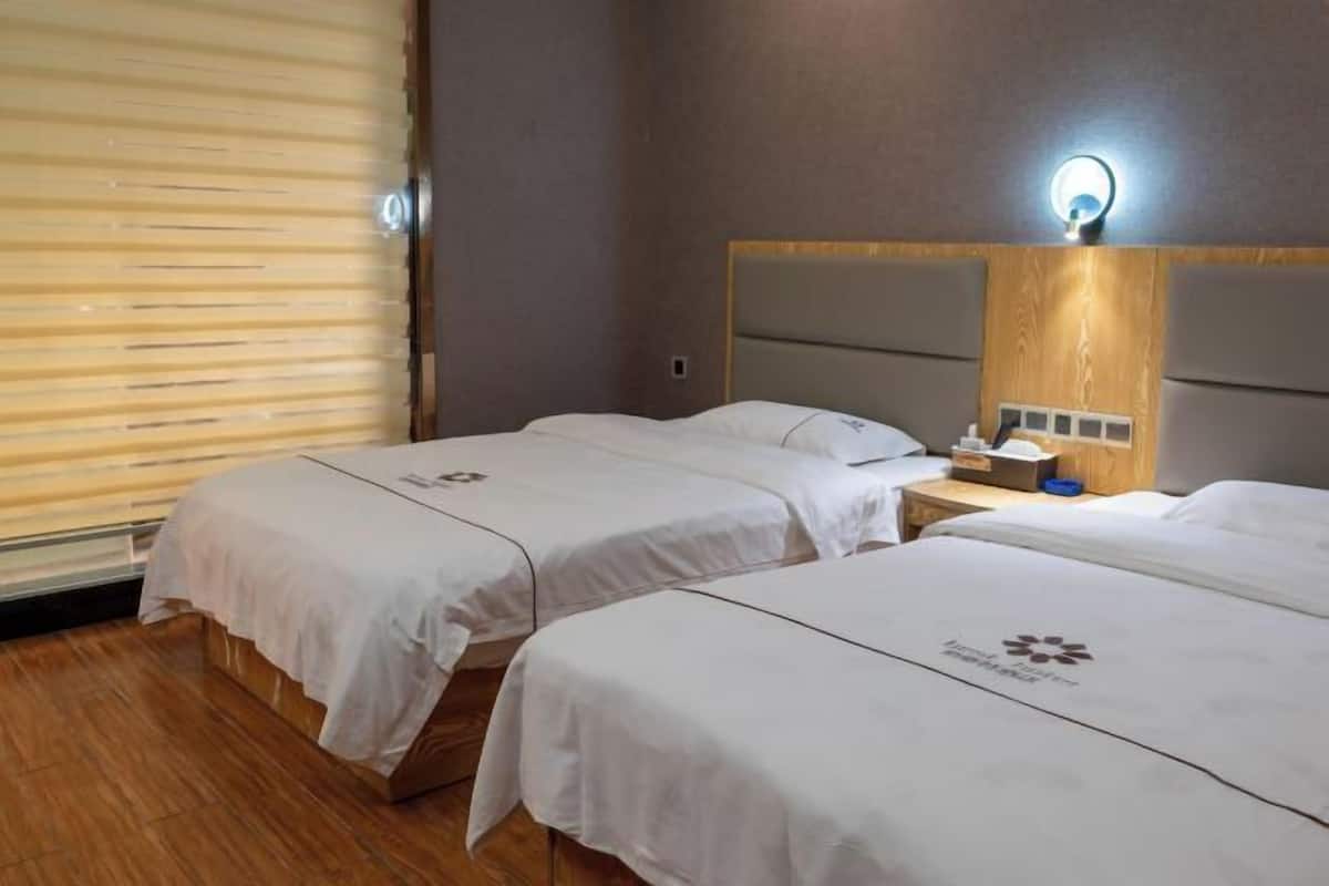 Een hotelkamer met twee bedden, een houten vloer, een grote spiegel en een nachtkastje met een lamp.