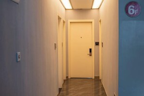 Un pasillo estrecho con una puerta al final, un interruptor de luz en la pared y un cartel con la indicación 6F a la derecha.
