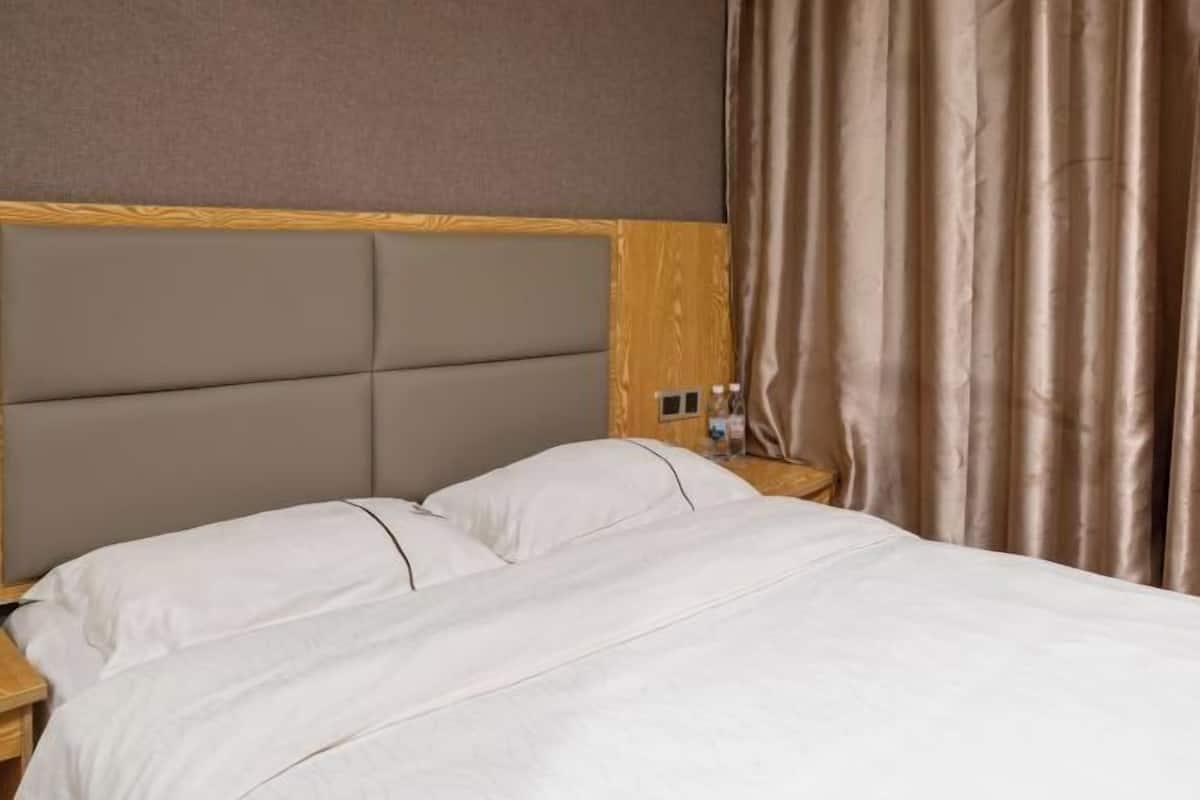 Een hotelkamer met een bed, hoofdbord, gordijnen en een nachtkastje.