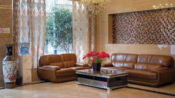 A lobby with a brown leather sofa, a coffee table with red flowers, and a patterned wall.