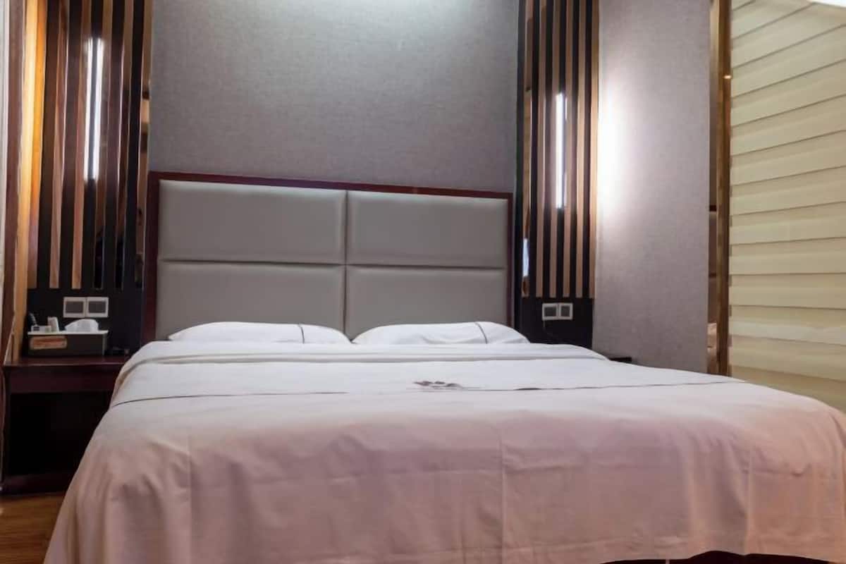 Een hotelkamer met een bed, nachtkastje en een paneel aan de muur.