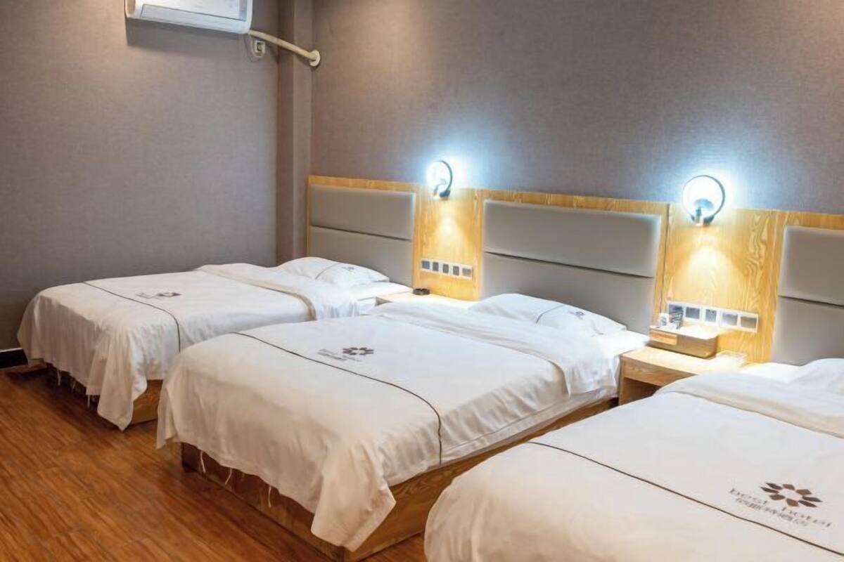 Een hotelkamer met drie eenpersoonsbedden, elk met hoofdeinde en nachtkastje.