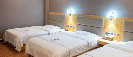A hotel room with three single beds, each with a headboard and bedside table.