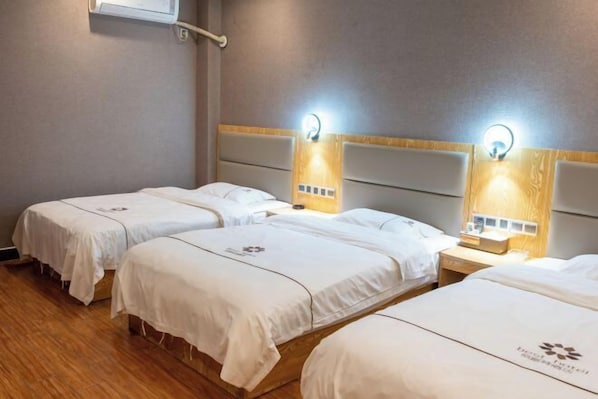 A hotel room with three single beds, each with a headboard and bedside table.