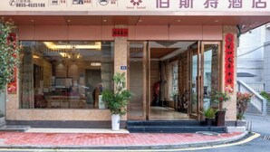 L’entrée d’un hôtel, avec une façade en verre, des plantes en pot et une enseigne rouge au-dessus de la porte.