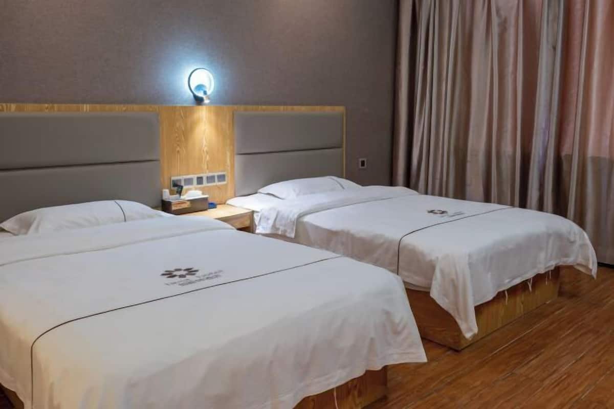 Een hotelkamer met twee bedden, een houten hoofdeinde, een nachtkastje met een lamp en een gordijn.
