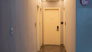 Un couloir étroit, avec une porte fermée au bout, un interrupteur sur le mur et une plaque indiquant le numéro de la pièce : 6F.