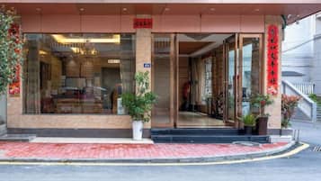 A hotel entrance with a glass facade, a red sign above the door, and potted plants on the steps.