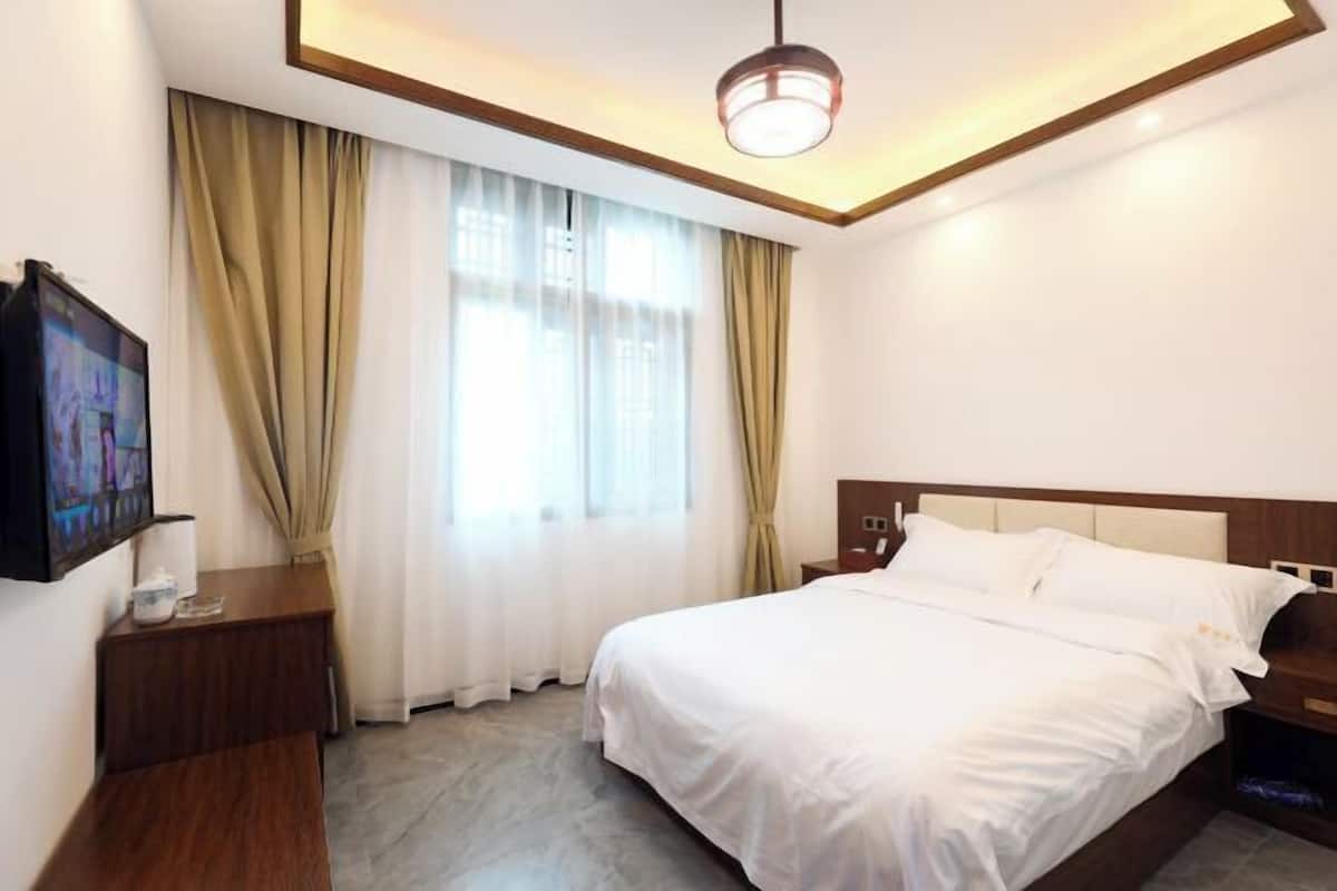 Une chambre d’hôtel avec un lit, un téléviseur posé sur un meuble, une table de chevet et une fenêtre avec des rideaux.