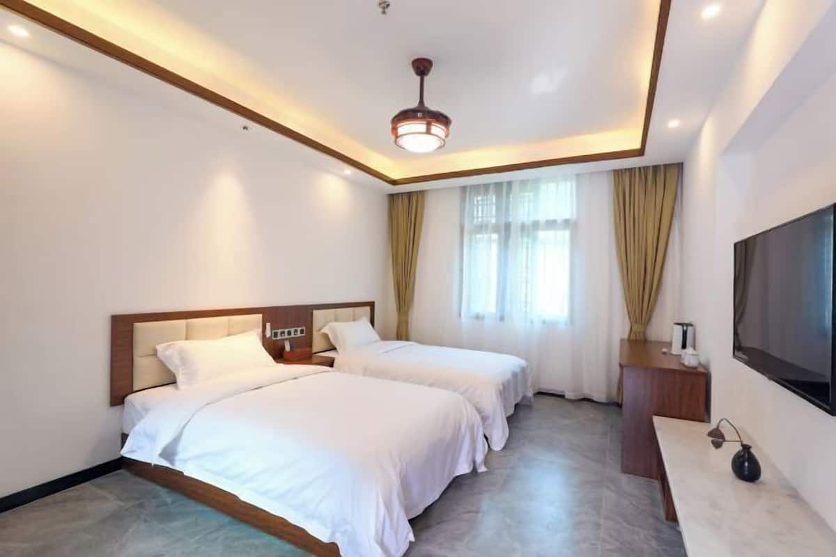 Une chambre d’hôtel avec deux lits, un téléviseur à écran plat, un bureau et un luminaire au plafond.