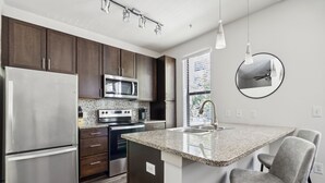 Una cocina moderna con armarios de madera oscura, electrodomésticos de acero inoxidable y una isla con encimera de granito y taburetes de bar.