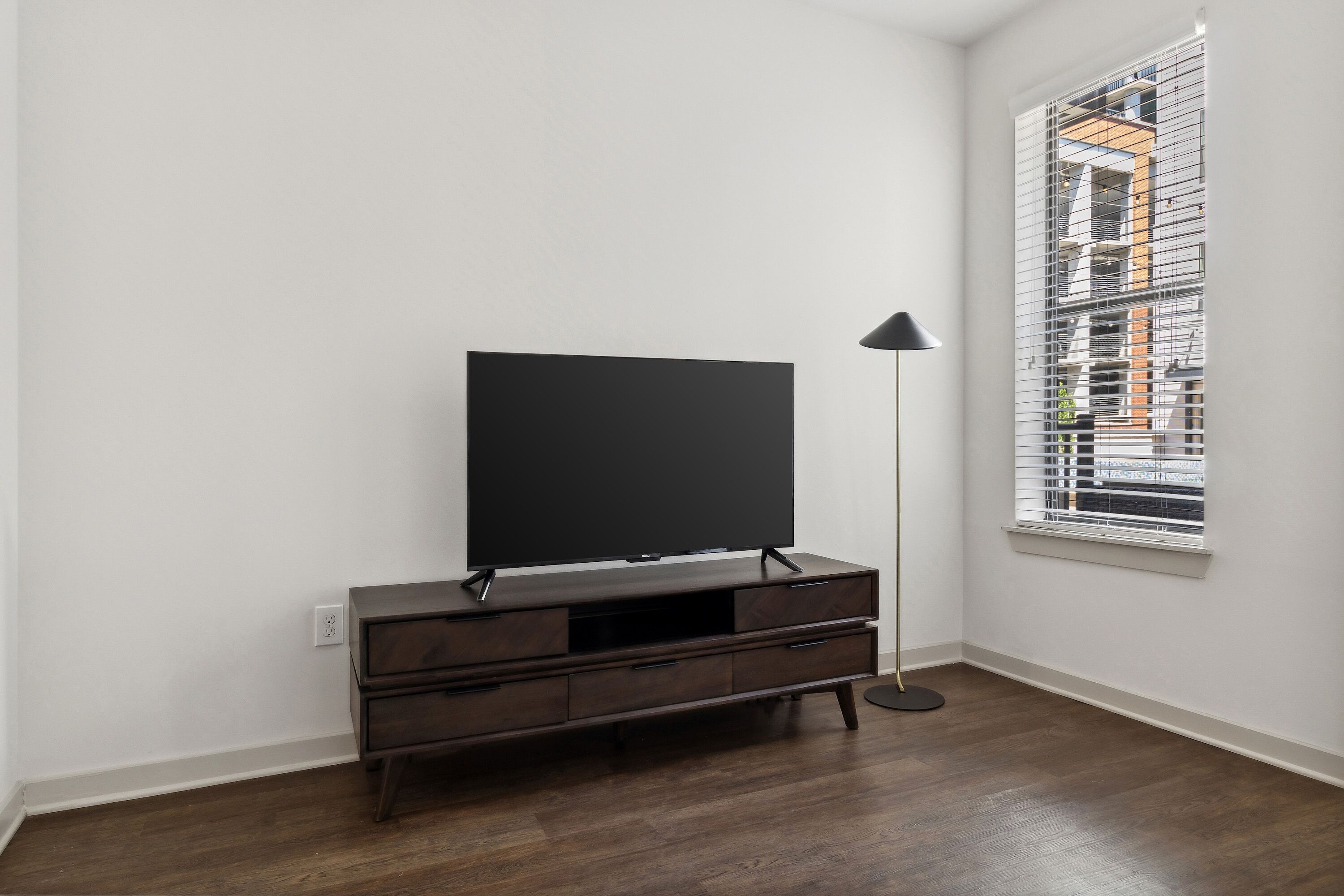 A room with a dark wooden TV stand, a flat-screen TV, and a floor lamp.