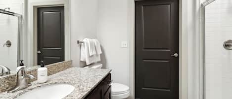 Une salle de bain avec un comptoir en granit, un lavabo blanc, une porte sombre et des toilettes blanches.