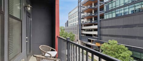 A balcony with wicker chairs, a red pillar, and a view of modern buildings.