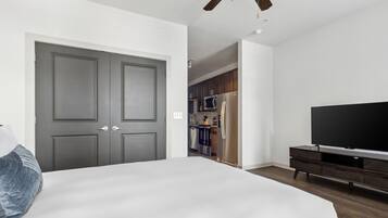 Een slaapkamer met een groot bed, een televisie, een garderobe en een keukenruimte zichtbaar door een geopende deur.