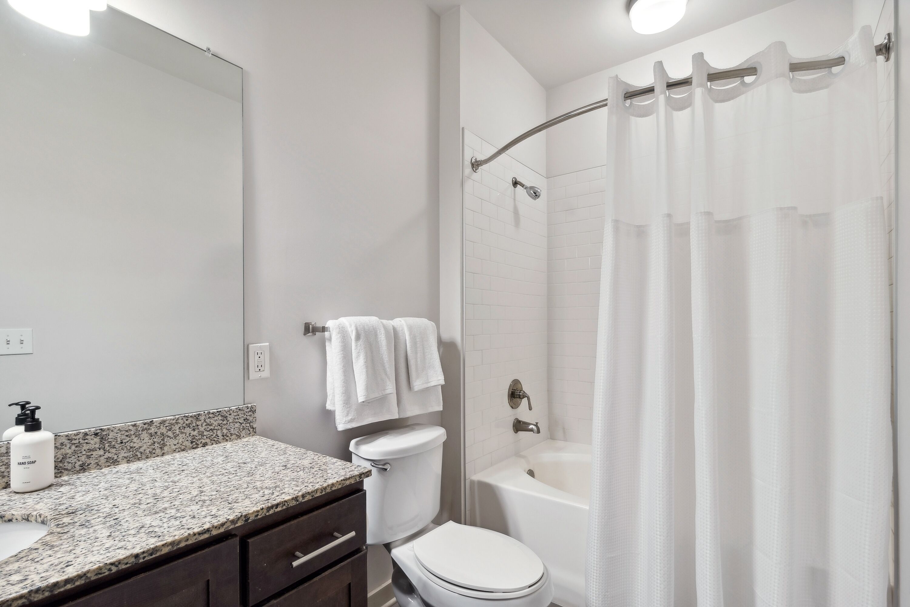 A bathroom with a granite countertop, white toilet, and a bathtub with a shower curtain.