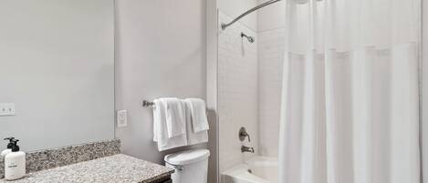 A bathroom with a granite countertop, white toilet, and a bathtub with a shower curtain.