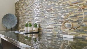 Cocina moderna con encimera de granito, salpicadero de mosaico y elementos decorativos como un espejo redondo y plantas en macetas.