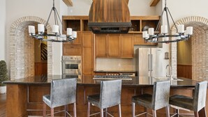 A kitchen with a central island, bar stools, a stainless steel range, and a brick wall. - Kasa Village District Raleigh (Raleigh)