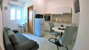 A compact living space with a sofa, a dining table with two chairs, a refrigerator, a microwave, and a small kitchen area with cabinets. - Apartment Tina (Ražanac)