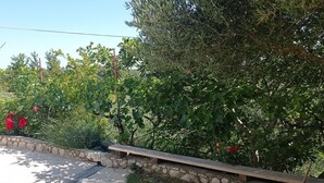 A stone wall with a bench, surrounded by lush greenery and trees. - Apartment Tina (Ražanac)