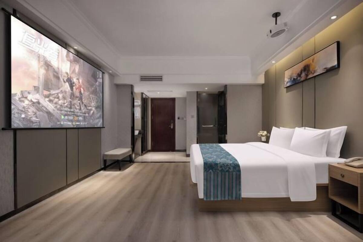 A modern hotel room with a large bed, a bedside table, a wall-mounted TV, and a door leading to another room.