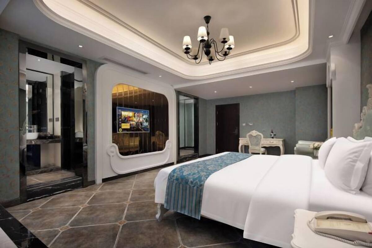 A modern hotel room with a large bed, a vanity with a mirror, and a television in the corner.