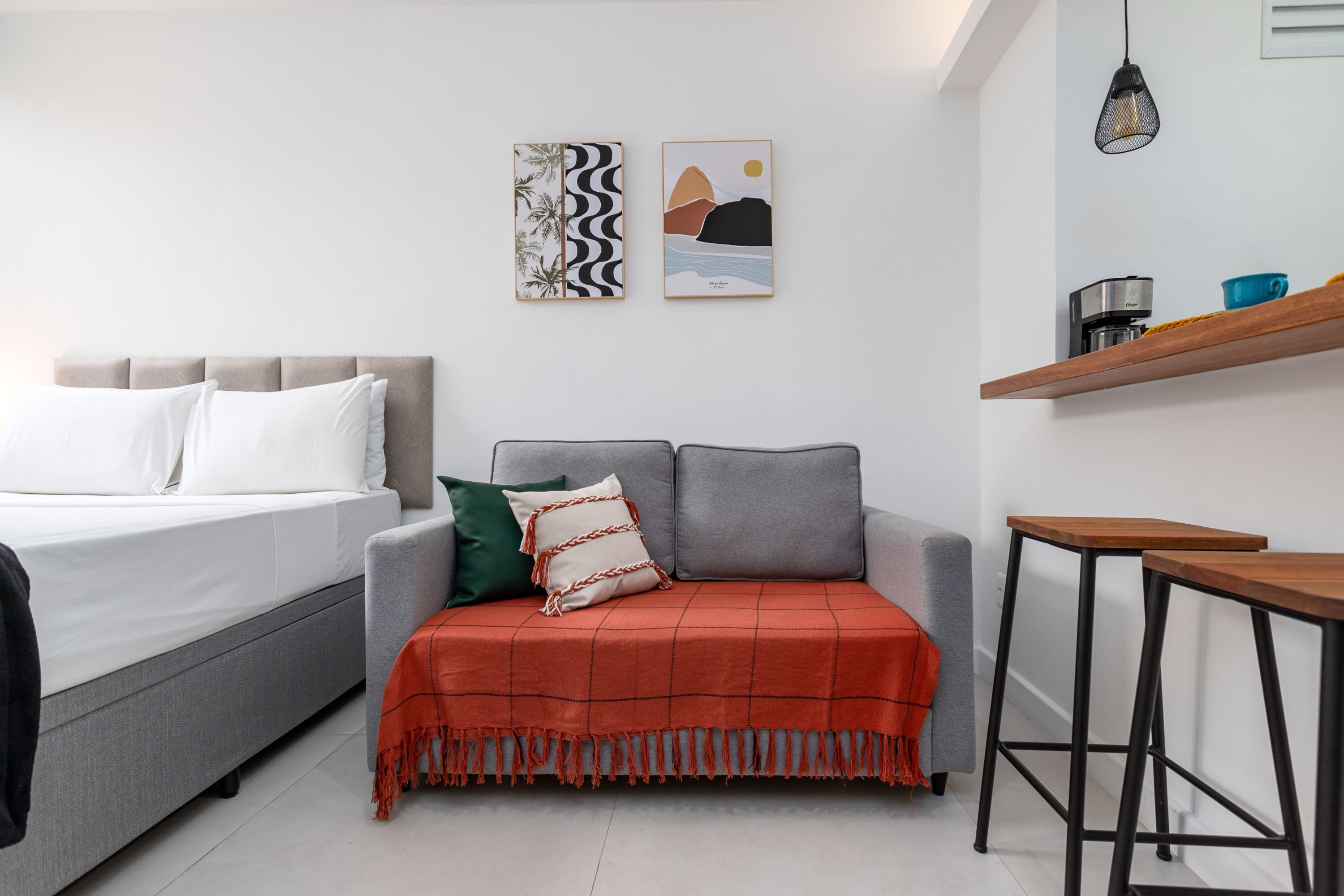 Une chambre moderne avec un lit, un canapé, une machine à café et une étagère sur laquelle se trouve une tasse.