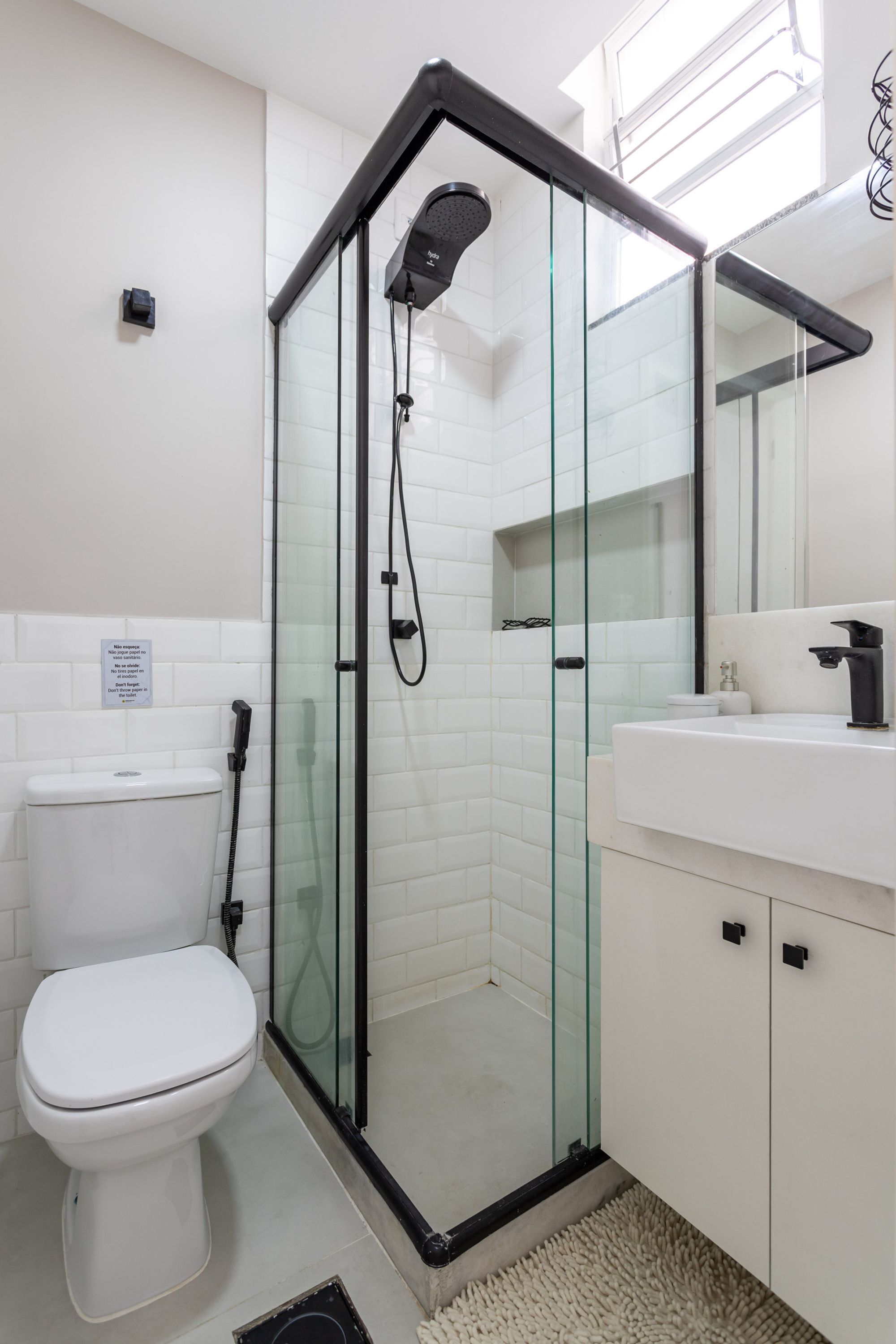 Ein modernes Badezimmer mit einer Glaskabinentrennung zur Dusche, weißen Fliesen, einer Toilette und einem Waschbecken mit Spiegel darüber.