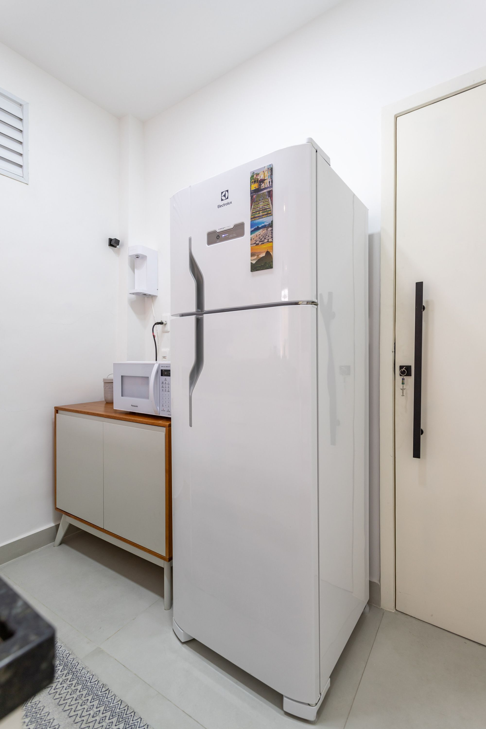 Una cocina compacta con un refrigerador blanco, microondas y un pequeño armario de madera.