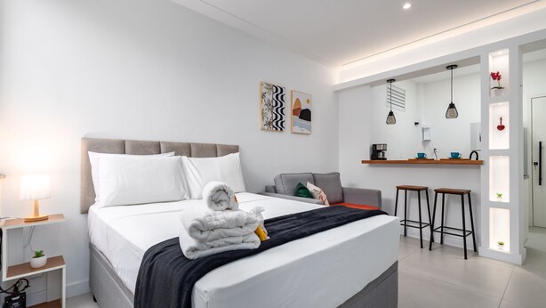 A modern hotel room with a neatly made bed, a small seating area, and a kitchenette. - 10 Minutes From Flamengo Beach Next to the Subway Ct404 (Rio de Janeiro)