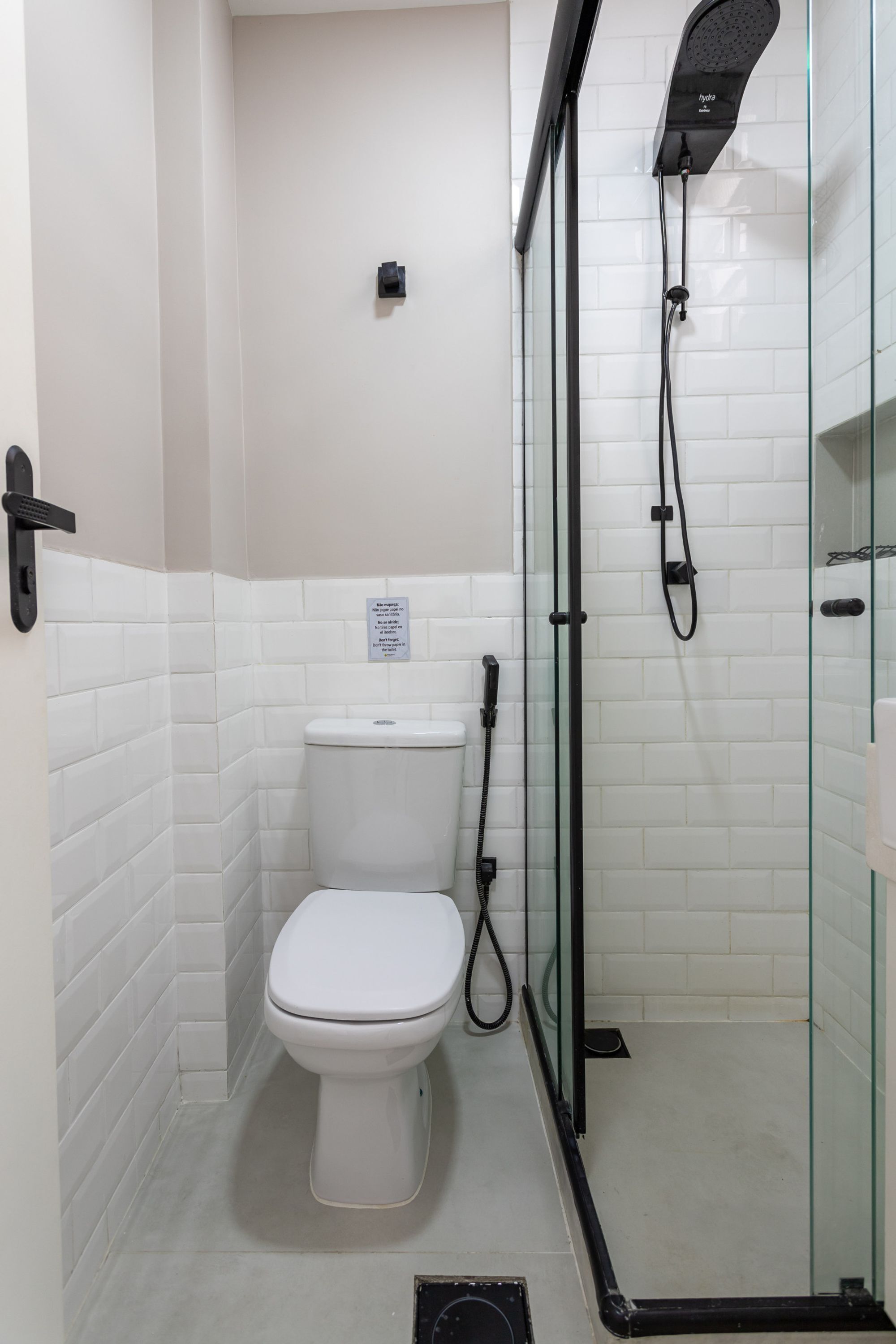 Un baño pequeño con inodoro blanco, ducha con mampara de vidrio y pared de azulejos blancos.