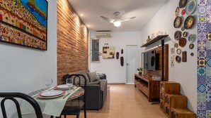 A dining area with a brick wall, a painting, and a TV in the background. - 7 Minutes From Copacabana Beach Stc504 (Rio de Janeiro)