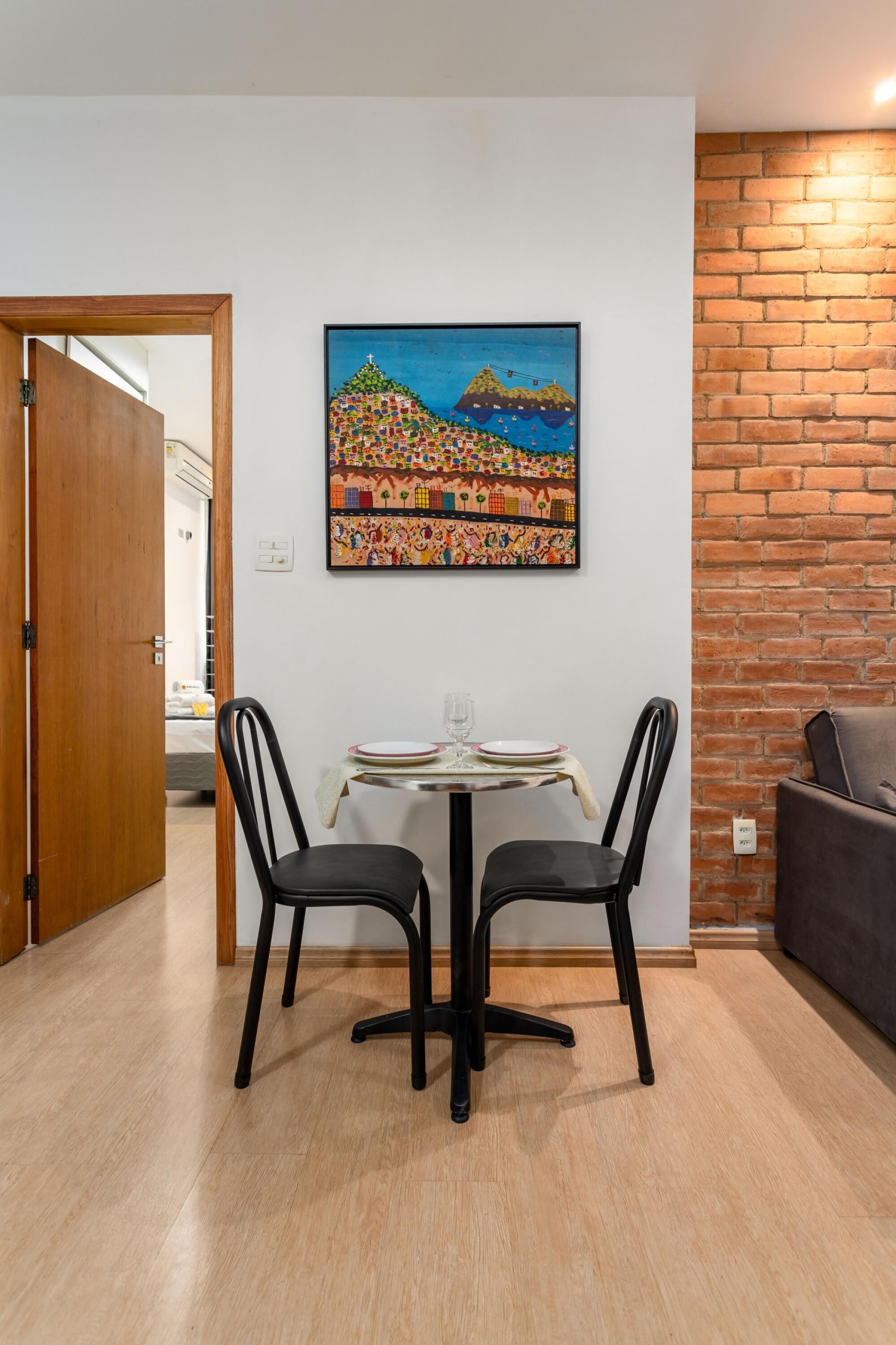 A dining area with a table and chairs, a painting on the wall, and a brick wall.