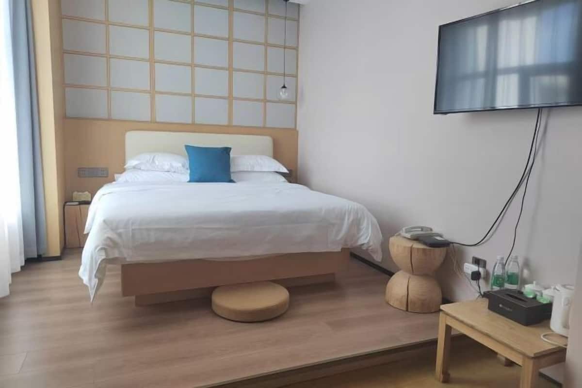 Una habitación de hotel moderna con una cama, televisión, mesita de noche y cabecero de madera.