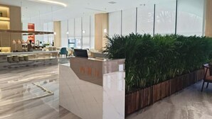 A modern reception area with a marble counter, a wooden planter with greenery, and a seating area with chairs.