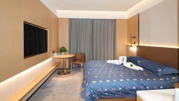 A hotel room with a bed, a desk, a chair, a TV, and a window with curtains.
