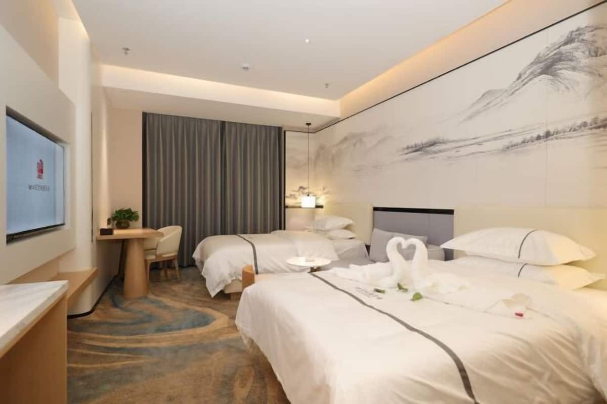 Habitación de hotel con dos camas, un escritorio, una silla, un televisor y un cuadro grande en la pared.