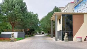 A street view with a building featuring a modern design, a statue, and a tree-lined background.