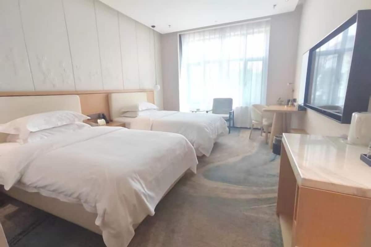 Habitación de hotel con dos camas, un escritorio, una silla, un ventanal grande y un espejo.