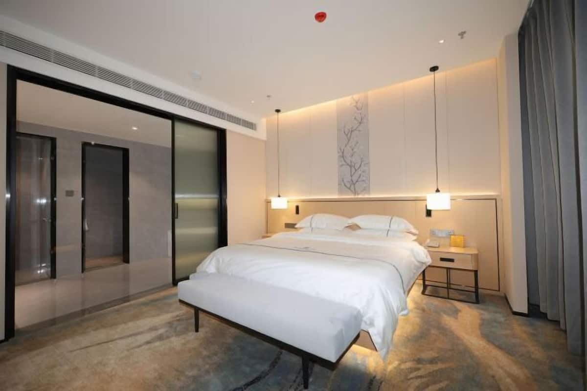 Una habitación de hotel moderna con una cama grande, mesitas de noche, un banco, una puerta corredera y una obra de arte colgada en la pared.