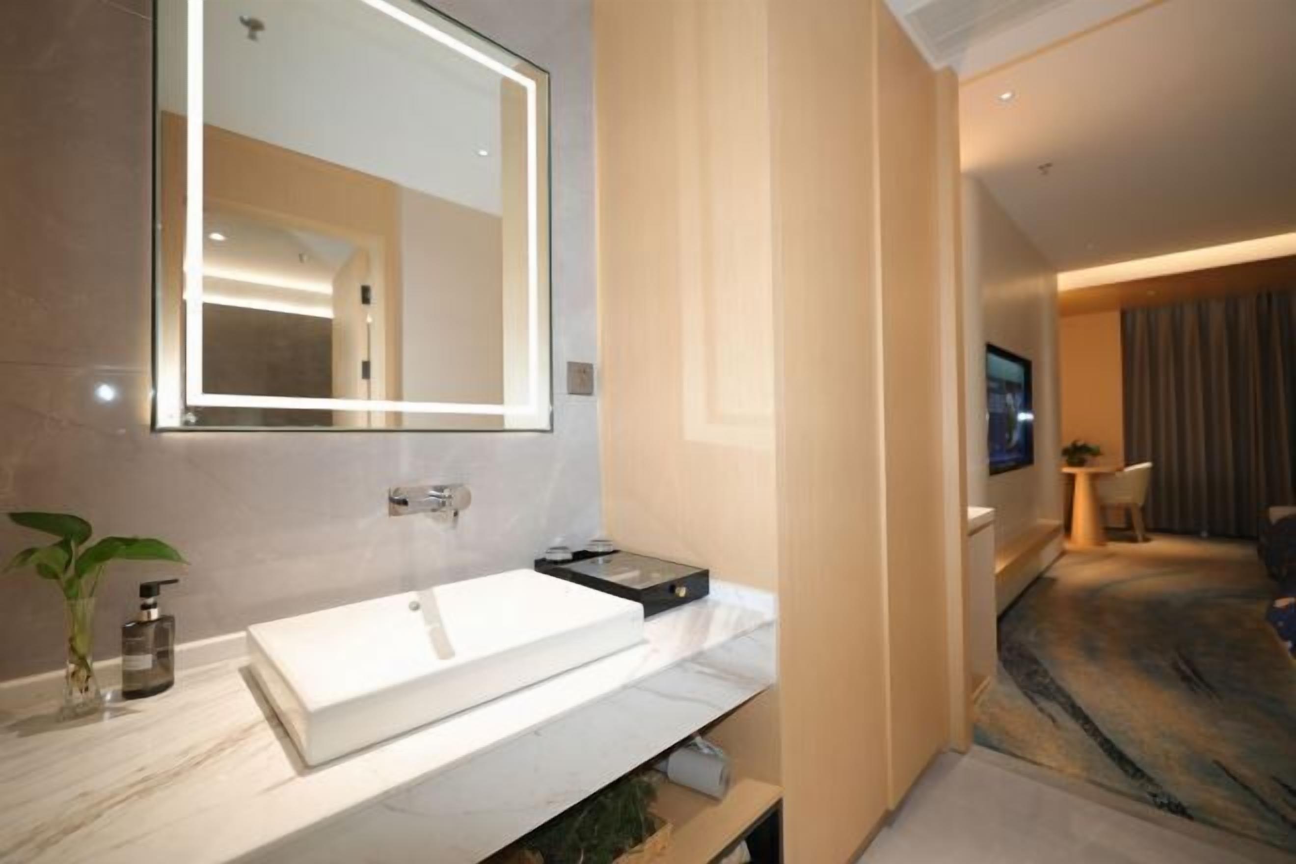 Een moderne badkamer met een grote spiegel, een witte wastafel en een kleine plant.