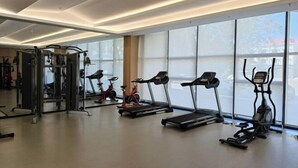 A modern gym with cardio machines, weightlifting equipment, and large windows offering a view of the outside.