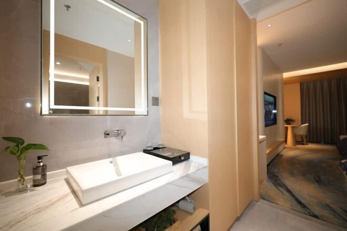 Un baño moderno con un espejo grande, un lavamanos blanco y una pequeña planta.
