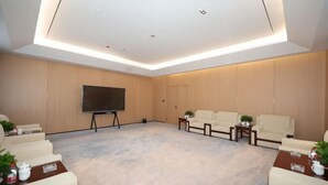 A conference room with a large flat-screen TV, beige sofas, and a carpeted floor. - Burqin Tourist Hotel (Burqin)