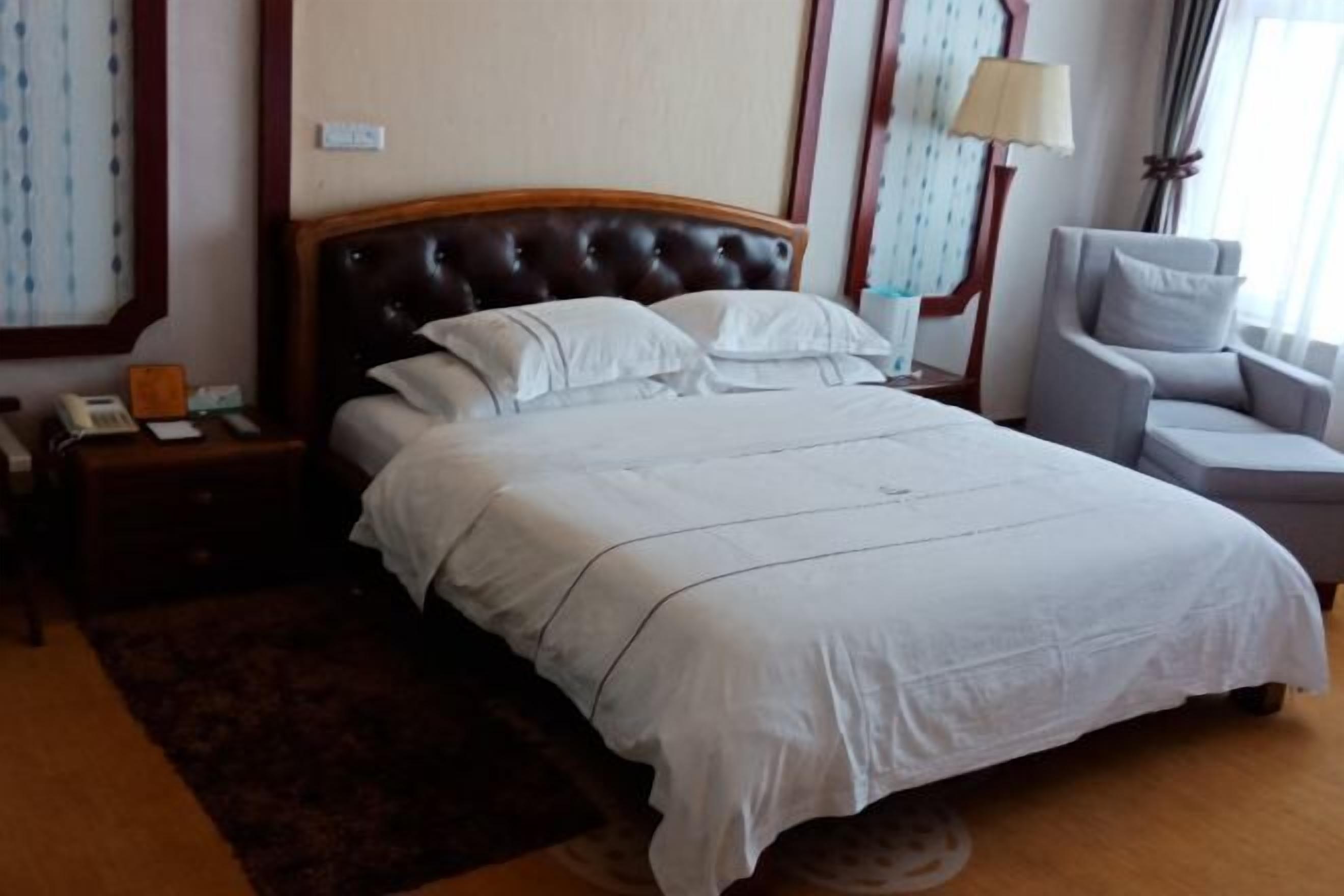 A neatly made bed with a headboard, a bedside table with a lamp, and a chair.
