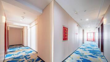 A hotel corridor with a patterned carpet, a red exit sign, and a door at the end.
